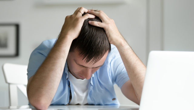 Portrait of man grabbing his head in despair near laptop