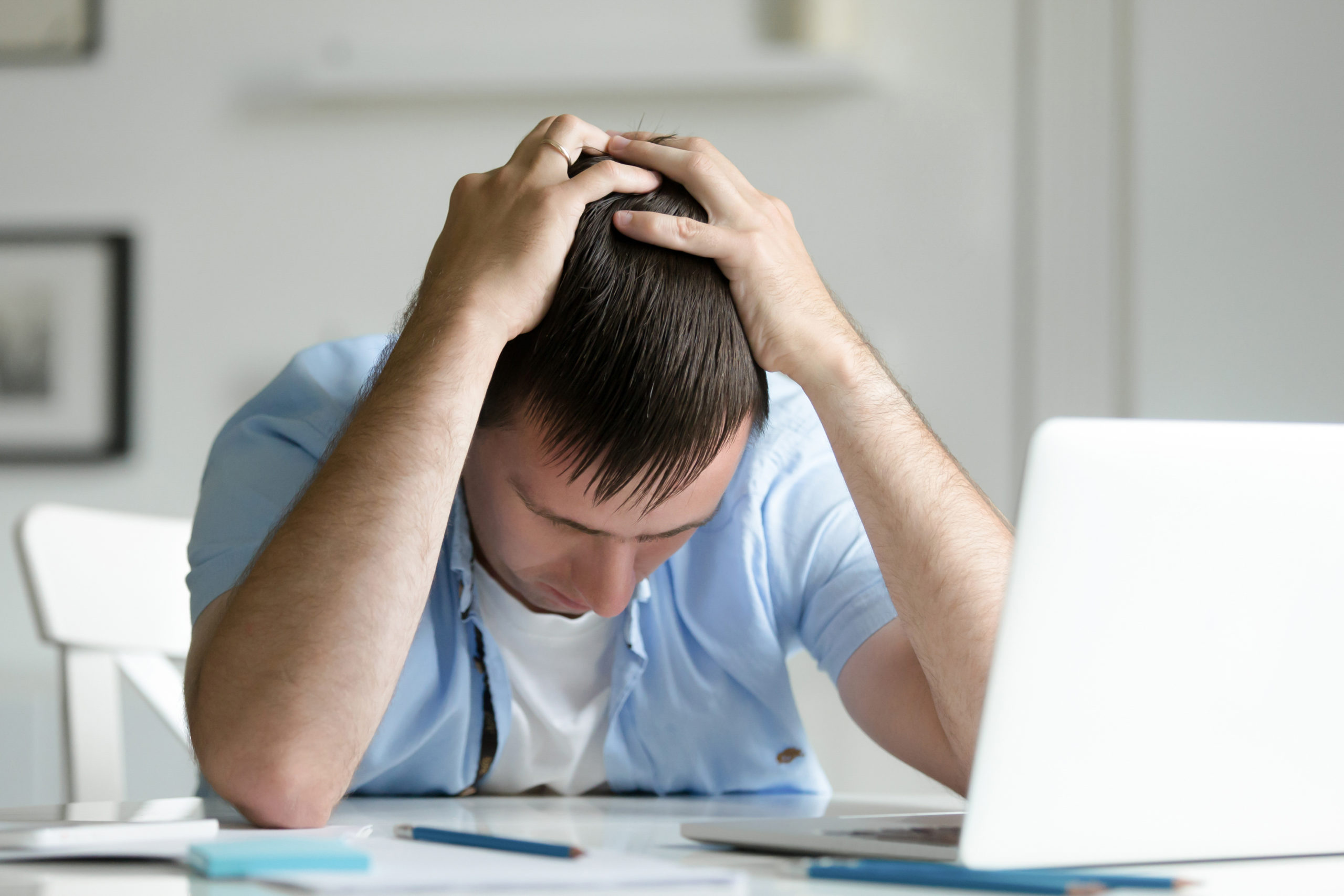 Portrait of man grabbing his head in despair near laptop