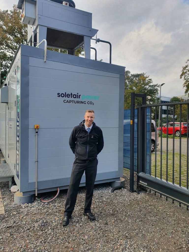 A man wearing black dress in front of a machine